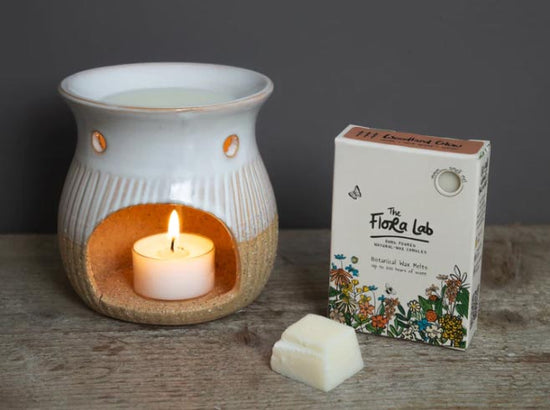Image of wax melt burner and Flora Lab illustrated packaging photographed on a wooden table in front of a grey background.