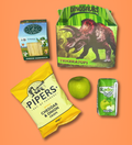 Assorted snacks including a cheese sandwich, cheddar & onion crisps, and apple juice on an orange background.