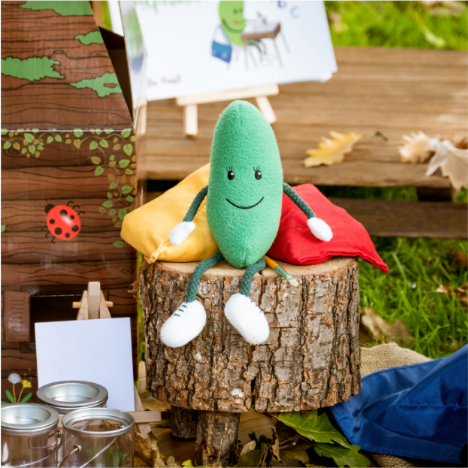A soft toy in the shape of a green bean sat on a log in a children's play area