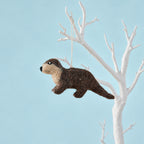 Handmade wool felt otter decoration with brown fur, small legs and a long tail, suspended from a white hanging loop.