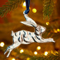 Silver leaping hare hanging decoration handcrafted from recycled aluminium and suspended from a blue velvet thread.