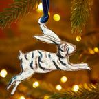 Silver leaping hare hanging decoration handcrafted from recycled aluminium and suspended from a blue velvet thread.