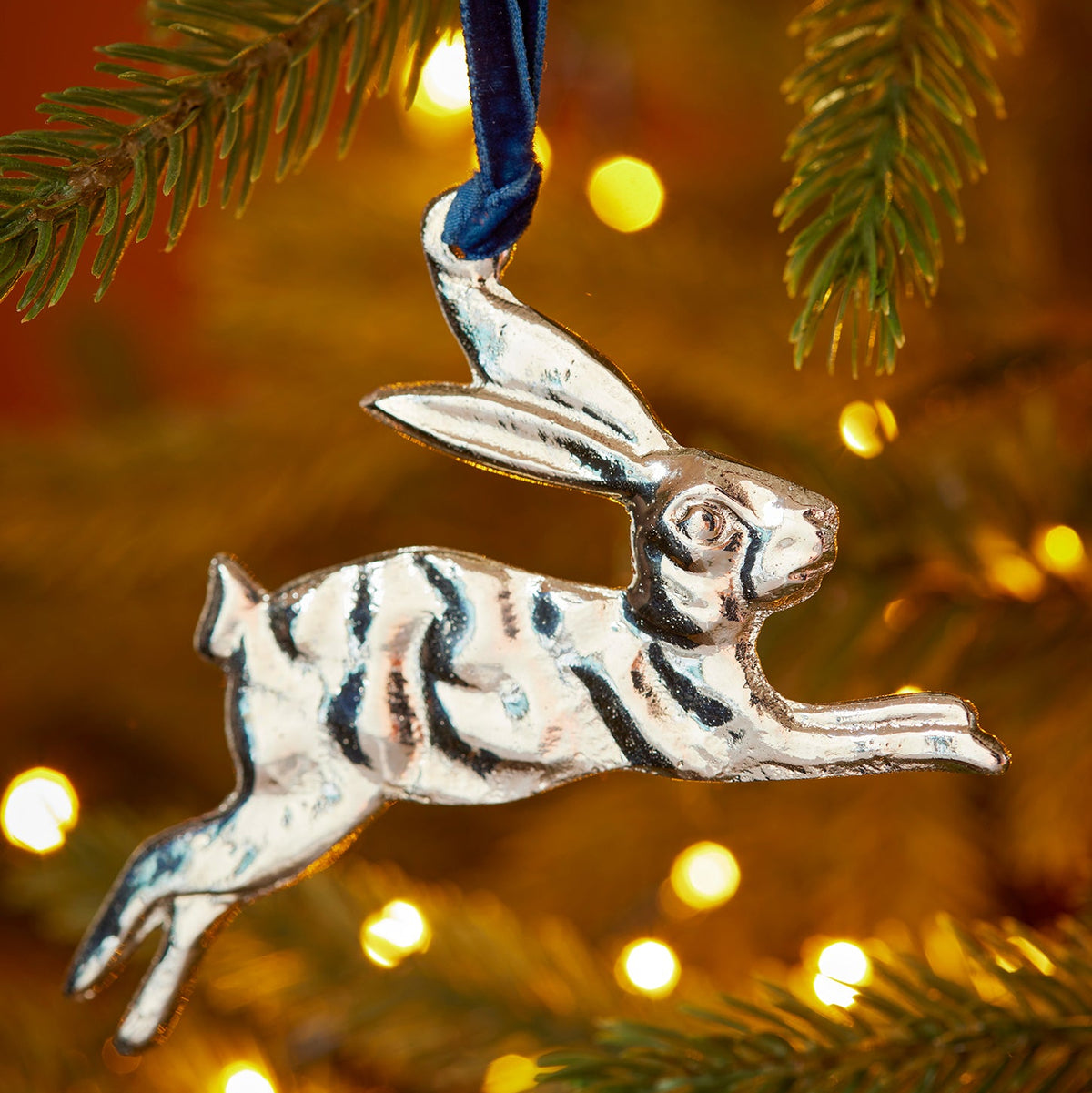 Silver leaping hare hanging decoration handcrafted from recycled aluminium and suspended from a blue velvet thread.