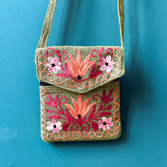 Green cotton back with strap. Red, orange and pink flowers embroidered across the front. Placed in front of a blue wall.