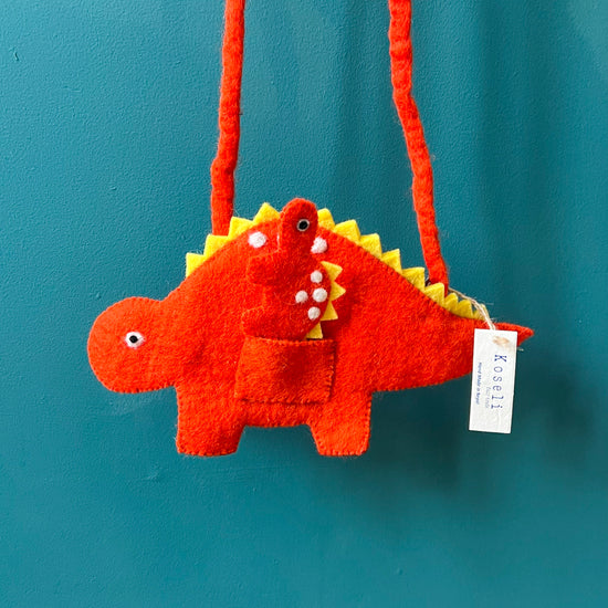 Red felt shoulder bag in the shape of a dinosaur hung in front of a blue wall.