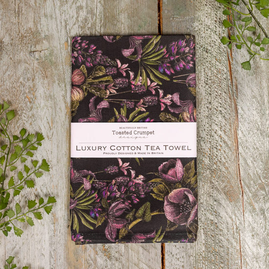 Tea towel folded into a rectangular shape with a white belly band with Toasted Crumpet branding. Photographed on a wooden surface.