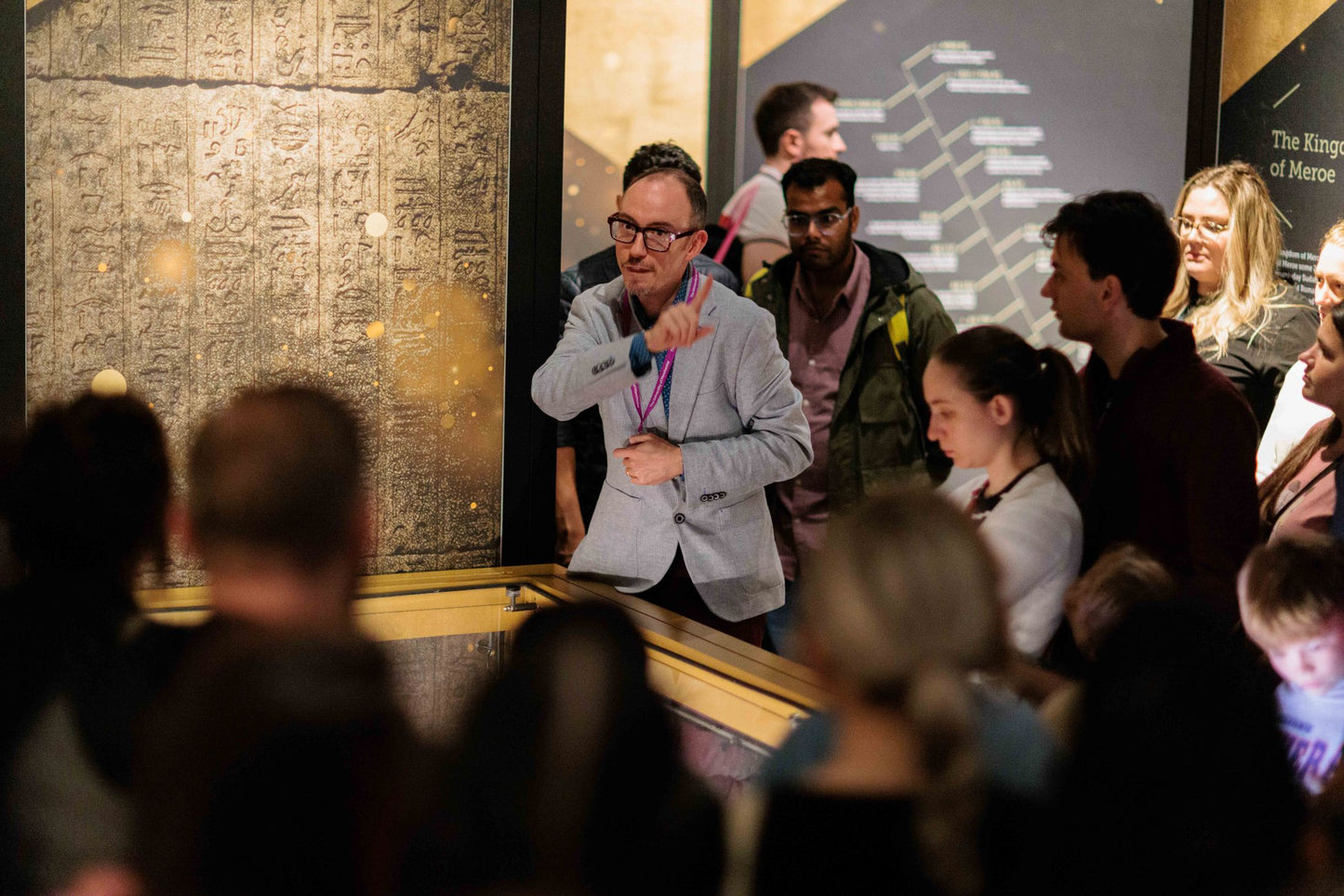 Tour photo of Dr Campbell Price during a presentation in the golden mummies exhibition with people standing around him.
