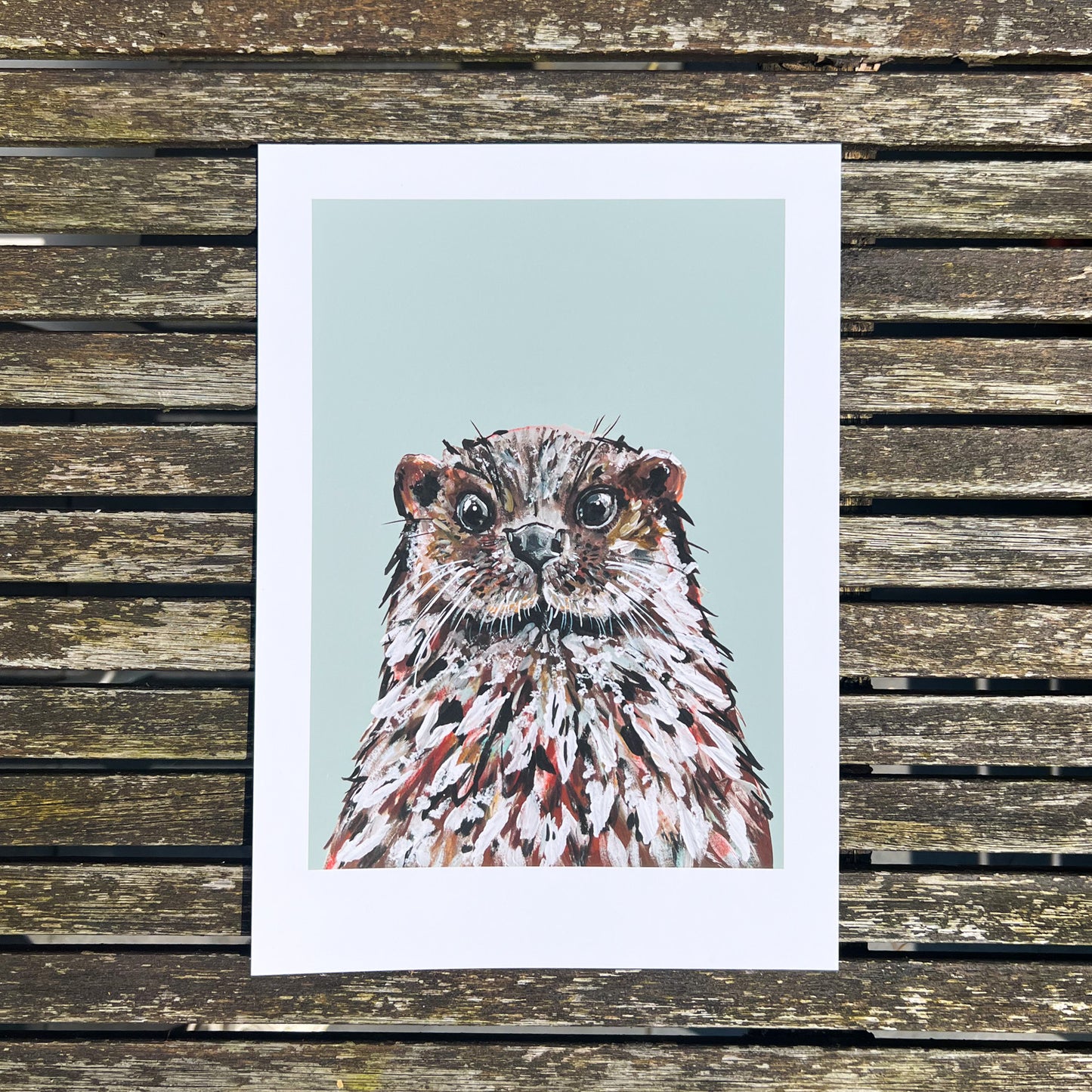 Print illustration of otter photographed from above on a wooden table.