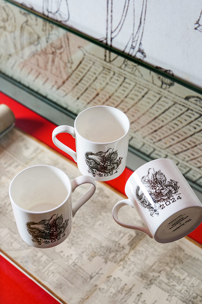 Two mugs sad side by side on a table, each with an illustration of a dragon