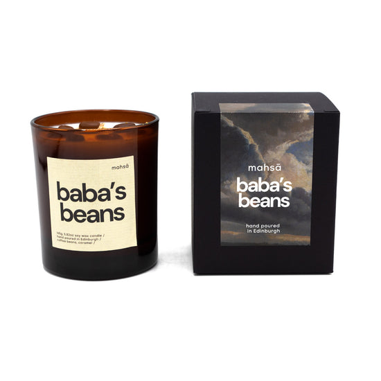 Candle with "baba's beans" written on the label. To the right is the box for the candle which includes Mahsa's logo and and a label with a photograph of the sky