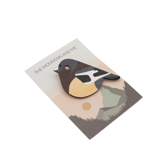 Wooden brooch in the shape of a Chaffinch bird against branded Mountain and Me packaging