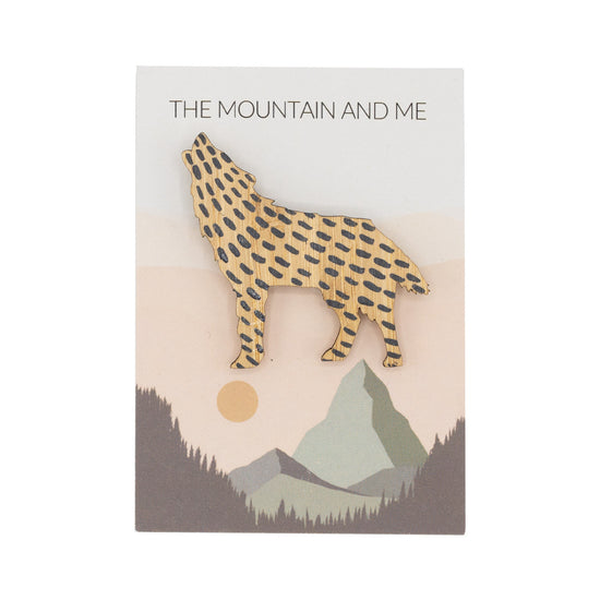 Wooden brooch in the shape of a howling wolf against The Mountain and Me branded backing card