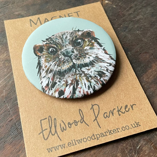 Lifestye photo of a round magnet with a otter illustration on it.