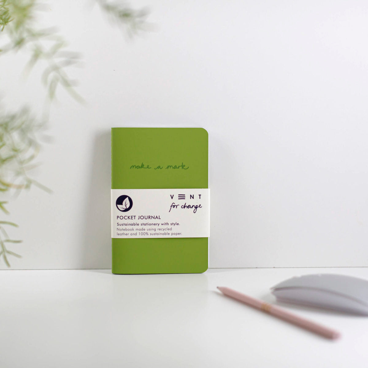 Green pocket journal with a white label on a light surface with a blurred plant in the background