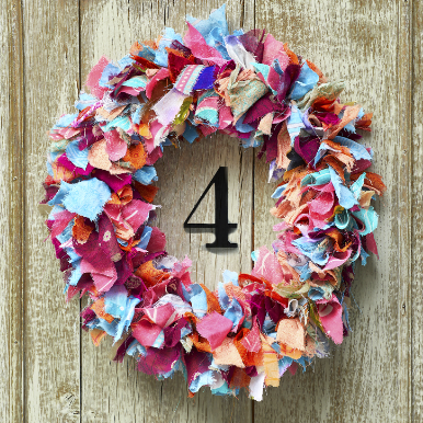 A close up of a multi-coloured wreath made out of recycled saris hung on a door.