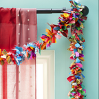 A colourful fabric garland hanging from a curtain rod. The garland is made of strips of recycled sari fabric in various colours and patterns.
