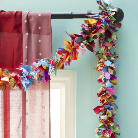 A colourful fabric garland hanging from a curtain rod. The garland is made of strips of recycled sari fabric in various colours and patterns.