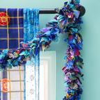 A blue fabric garland hanging from a curtain rod. The garland is made of strips of recycled sari fabric.