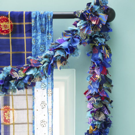 A blue fabric garland hanging from a curtain rod. The garland is made of strips of recycled sari fabric.