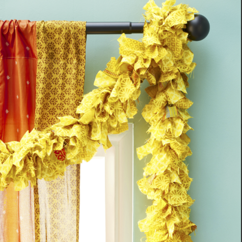 A yellow fabric garland hanging from a curtain rod. The garland is made of strips of recycled sari fabric in various patterns.