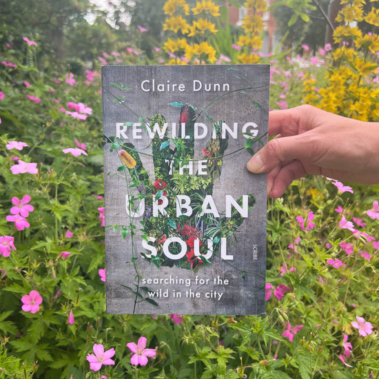 Rewilding The Urban Soul Book held up against a garden backdrop.