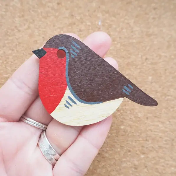 A hand-painted wooden robin decoration, held in a hand. The robin has a black head, red breast, brown body, and white belly.