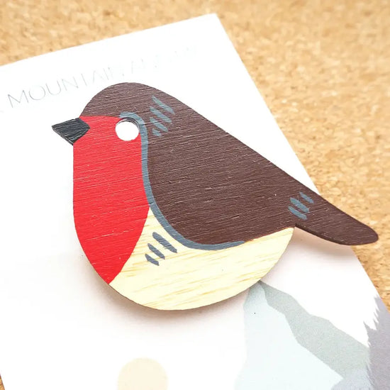 A hand-painted wooden robin decoration, on backing card. The robin has a black head, red breast, brown body, and white belly.