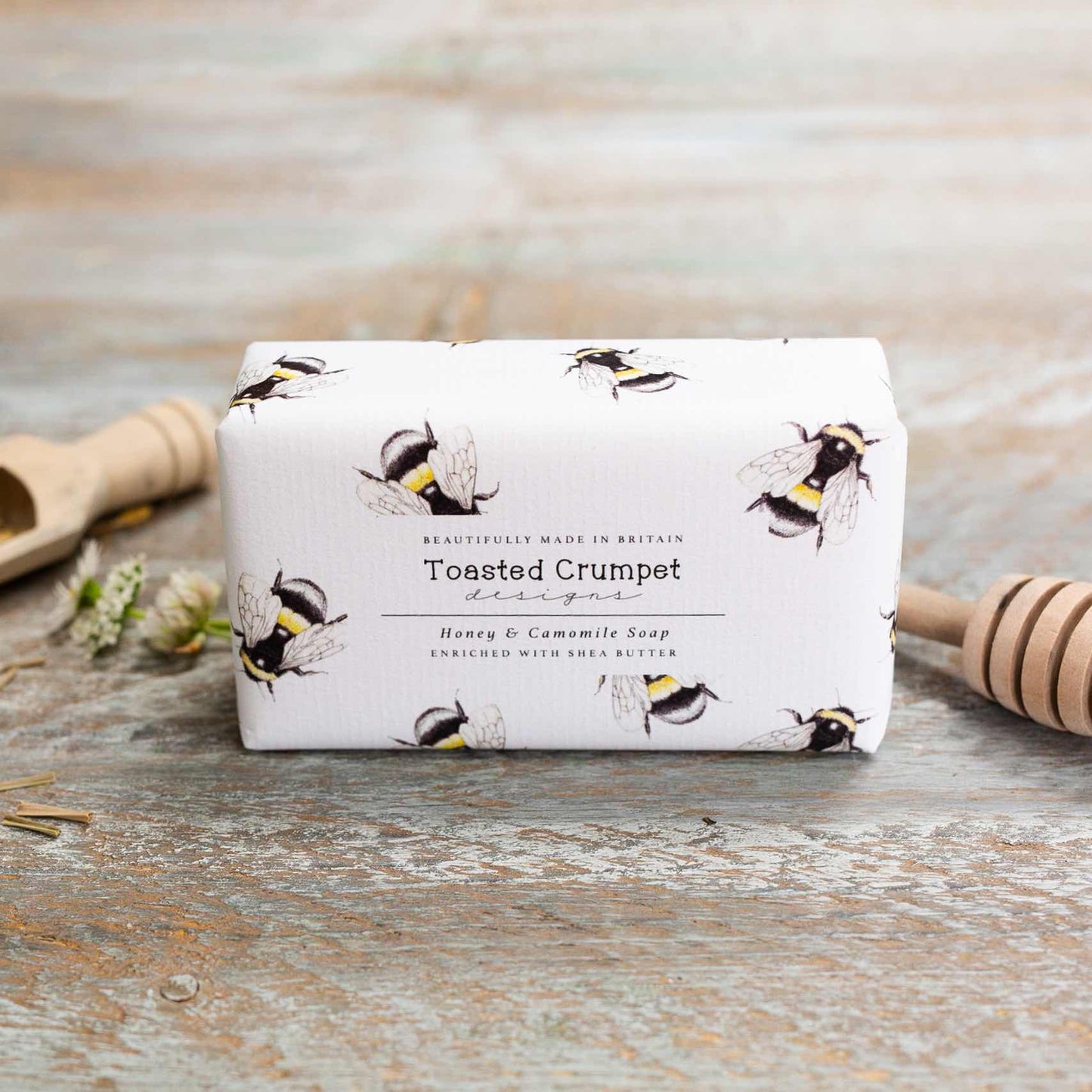 Rectangular soap in white packaging with a bee pattern. Photographed on a wooden surface. 