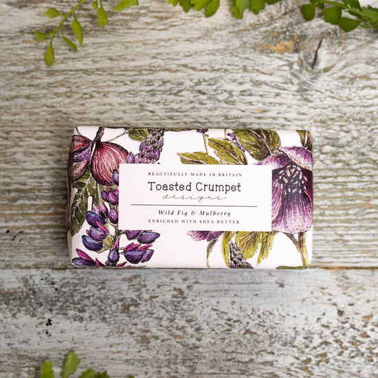 Rectangular soap in purple, white and green floral packaging with Toasted Crumpet branded label. Photographed against wooden surface.