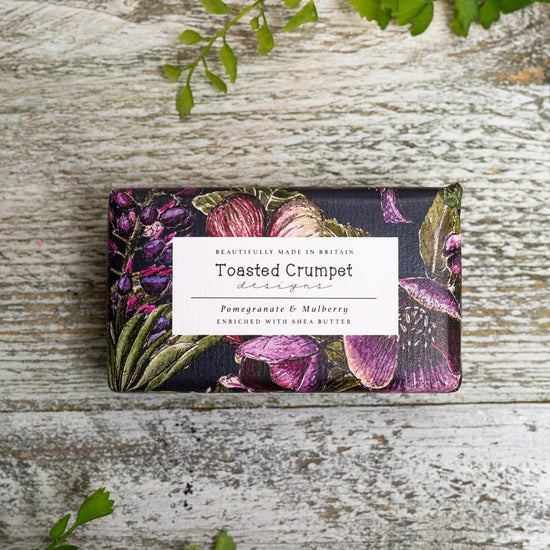 Rectangular soap in purple, black and green floral packaging with Toasted Crumpet branded label. Photographed birds-eye view on a wooden surface.