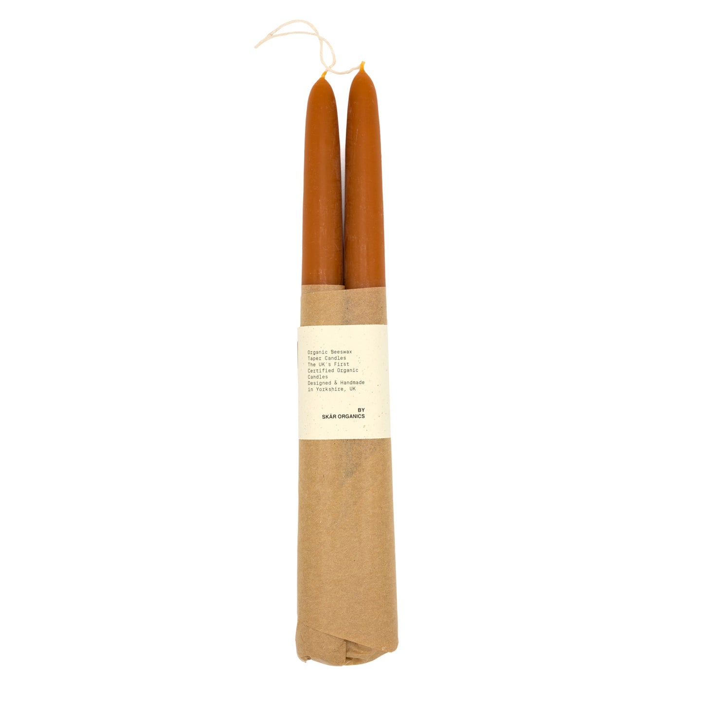 A pair of organic beeswax candles wrapped in brown paper with text that says “Skar Organics Designed & Handmade Candles”  on a white background.