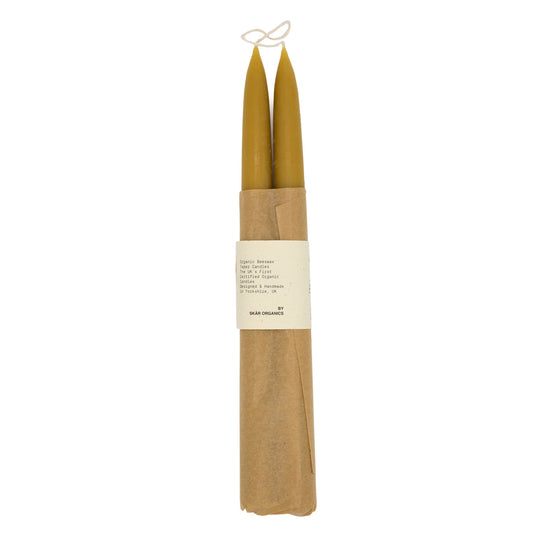 A pair of organic beeswax candles wrapped in brown paper with text that says “Skar Organics Designed & Handmade Candles”  on a white background.