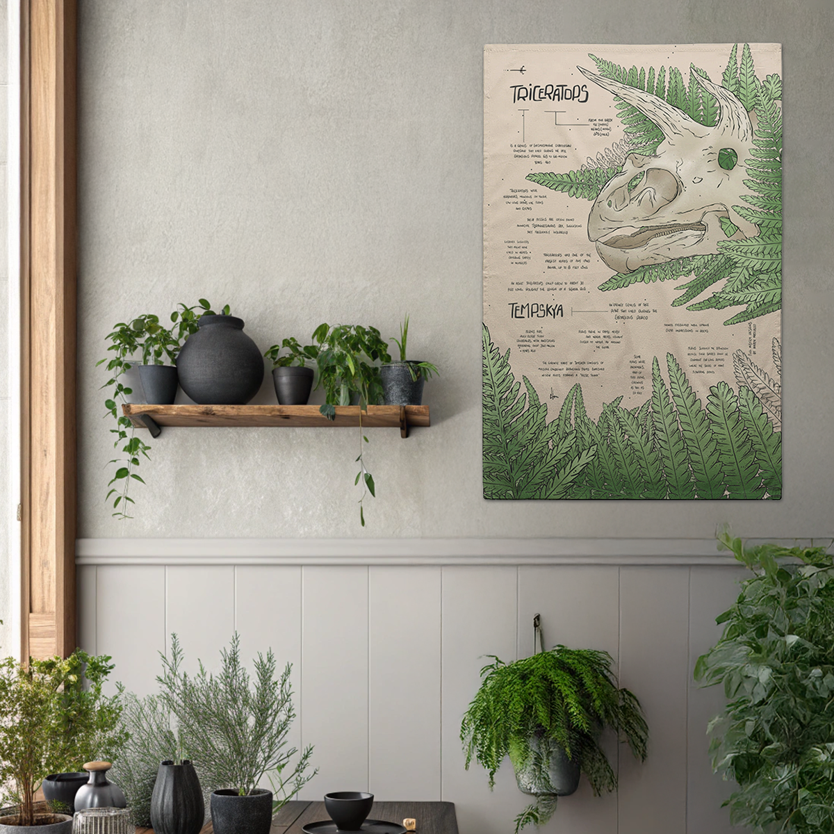 Tea towel hanging on a wall of a triceratops skeleton with plants and a shelf below.