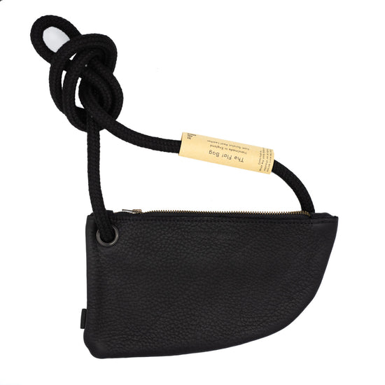 A black leather crossbody bag with a rope strap. The bag has a curved shape and a zipper closure. A tag is attached to the strap reads with product info.