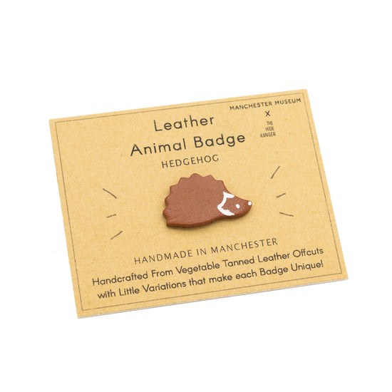 Handmade and hand painted badge in the shape of a hedgehog, against a brown backing card with The Hide Ranger's logo and product information.