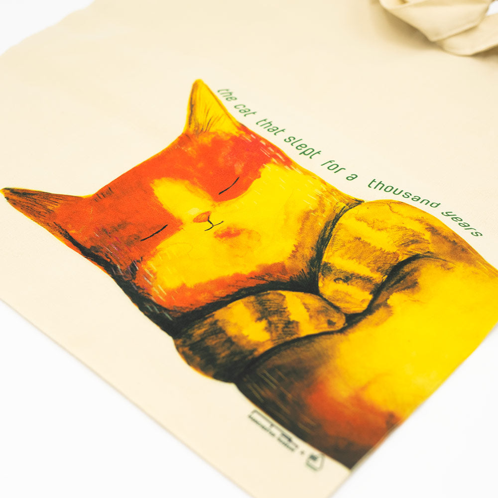 Sleeping cat illustration on a tote bag with text.