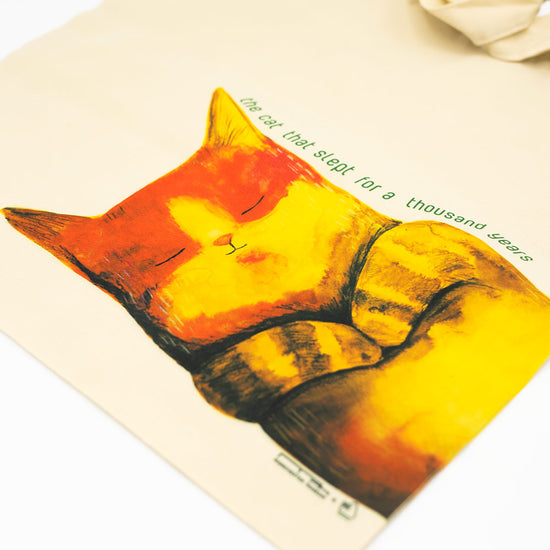 Sleeping cat illustration on a tote bag with text.