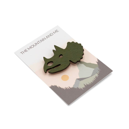 Wooden brooch shaped like a triceratops head on branded 'The Mountain and Me' backing card.