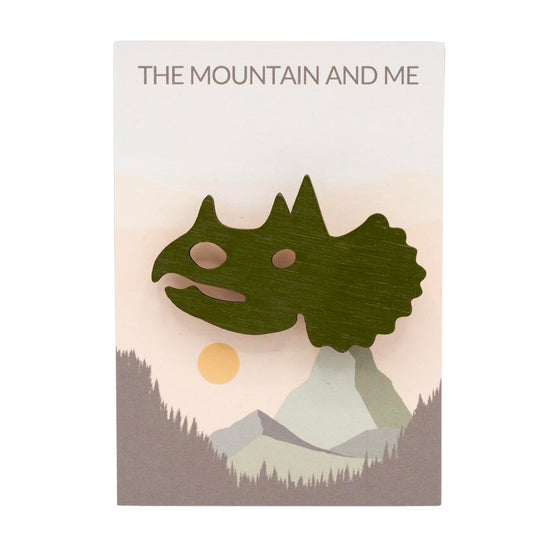 Wooden brooch shaped like a triceratops head on branded 'The Mountain and Me' backing card.