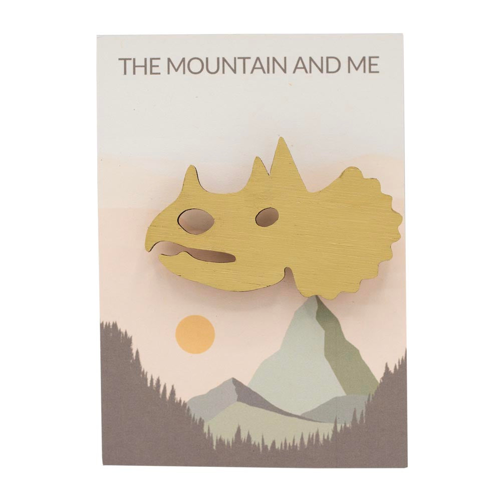 Wooden brooch shaped like a triceratops head on branded 'The Mountain and Me' backing card.