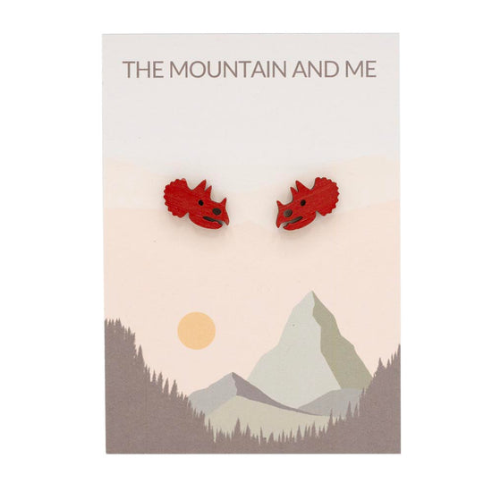 Red triceratops-head earrings on a card with mountain design and 'The Mountain and Me' text