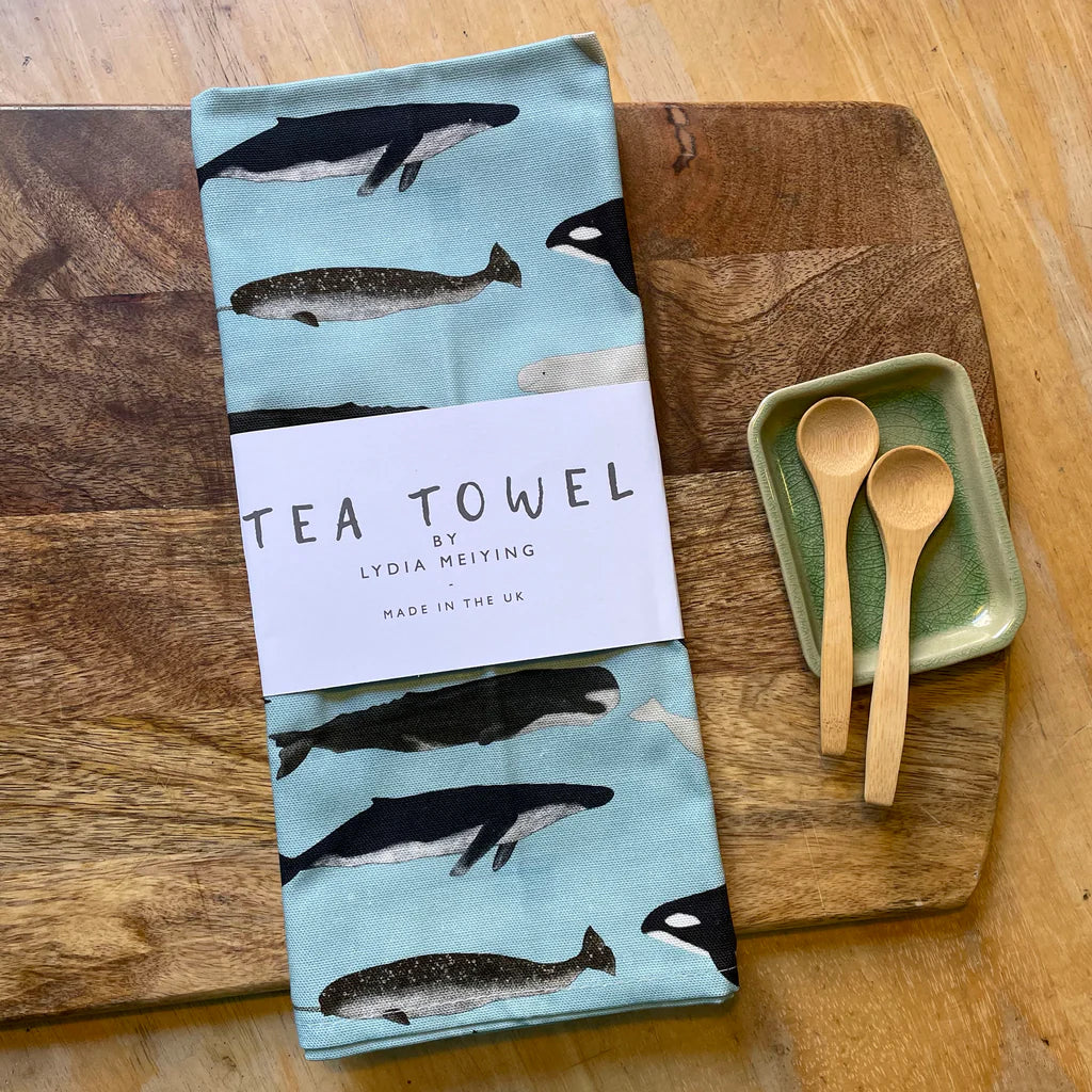 Tea towel with whale pattern on a wooden surface with wooden spoons and a green dish.