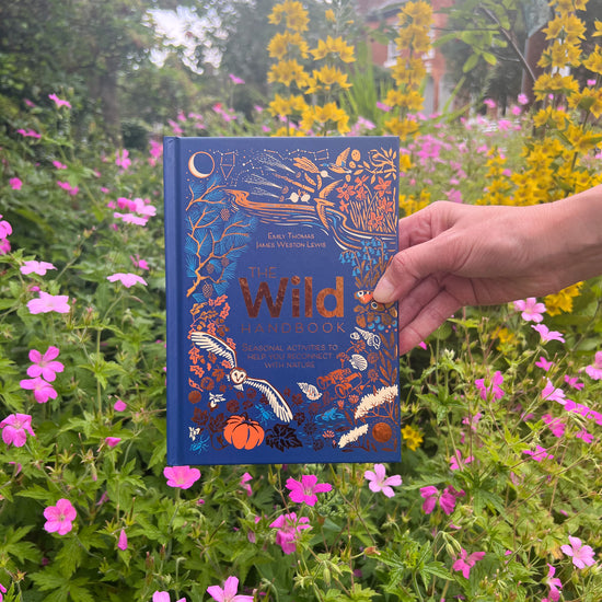 Wild Handbook held up against a garden backdrop