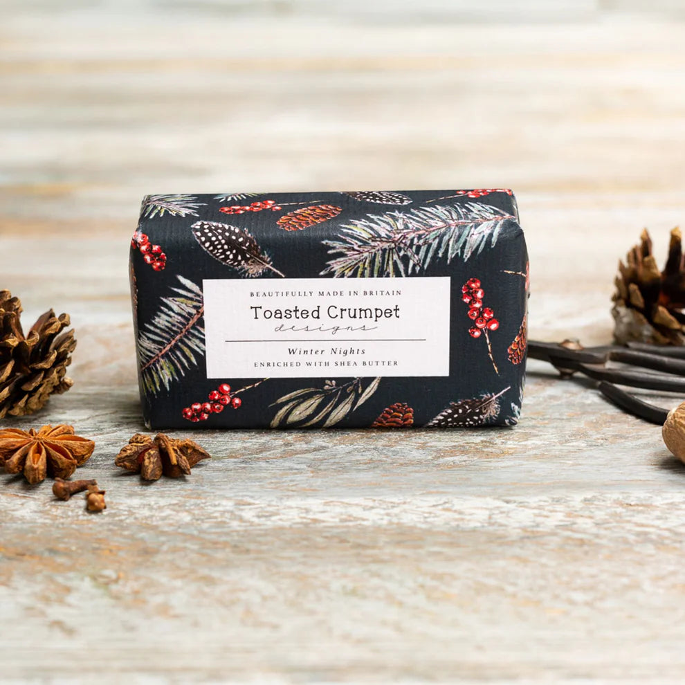 Soap bar with navy botanical packaging, presented on a wooden surface
