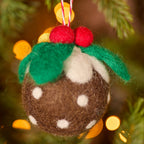Handmade wool felt Christmas pudding decoration with white icing, red holly berries and green felt leaves, hanging from a loop for festive tree display.