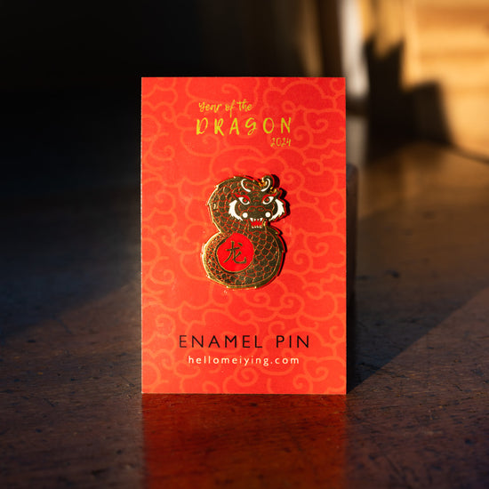 Gold pin in the shape of a dragon photographed on Lydia Leiying red branded backing card