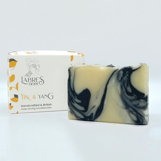 A rectangular bar of soap with a white base and swirls of black. The soap is resting inside a white cardboard box with a black and white label.