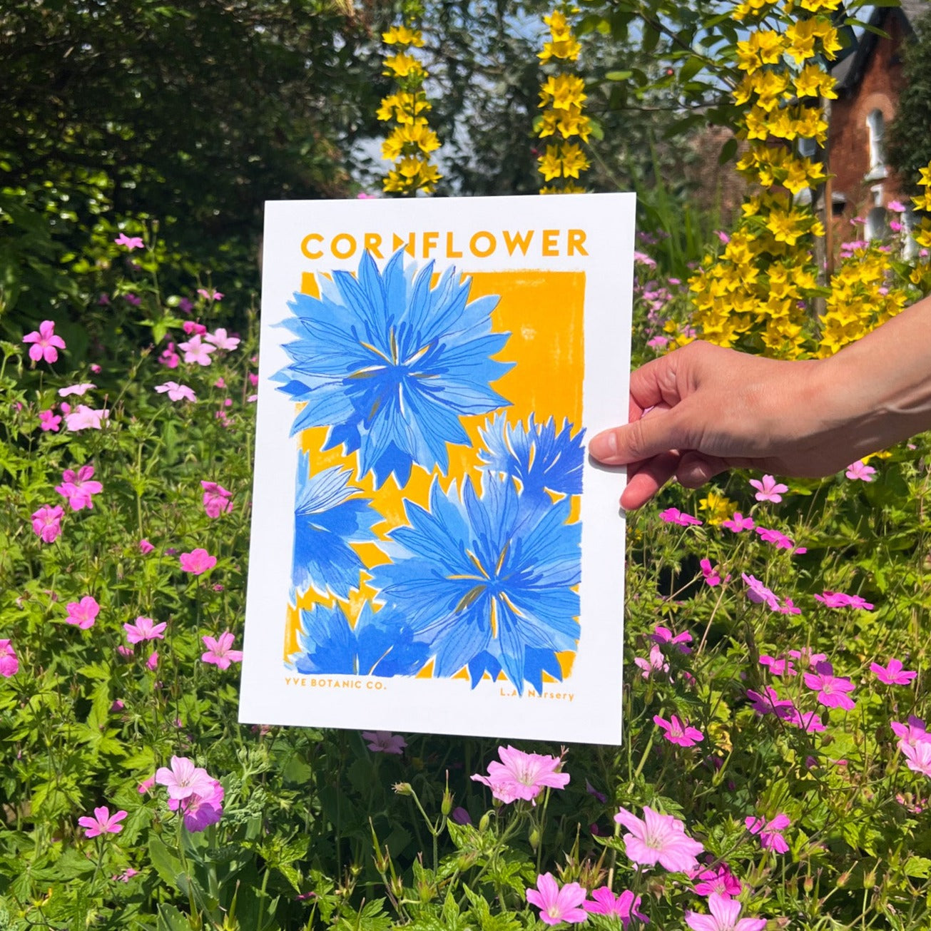 A person holding a print in front of a garden backdrop. 