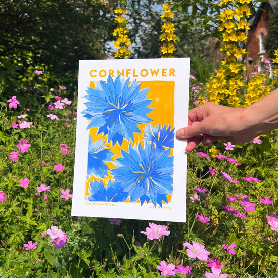 A person holding a print in front of a garden backdrop. 