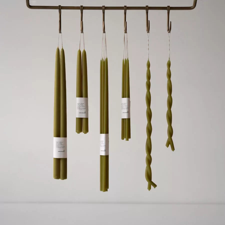 A bunch of green candles in various shapes and sizes hanging from hooks on a shelf.  